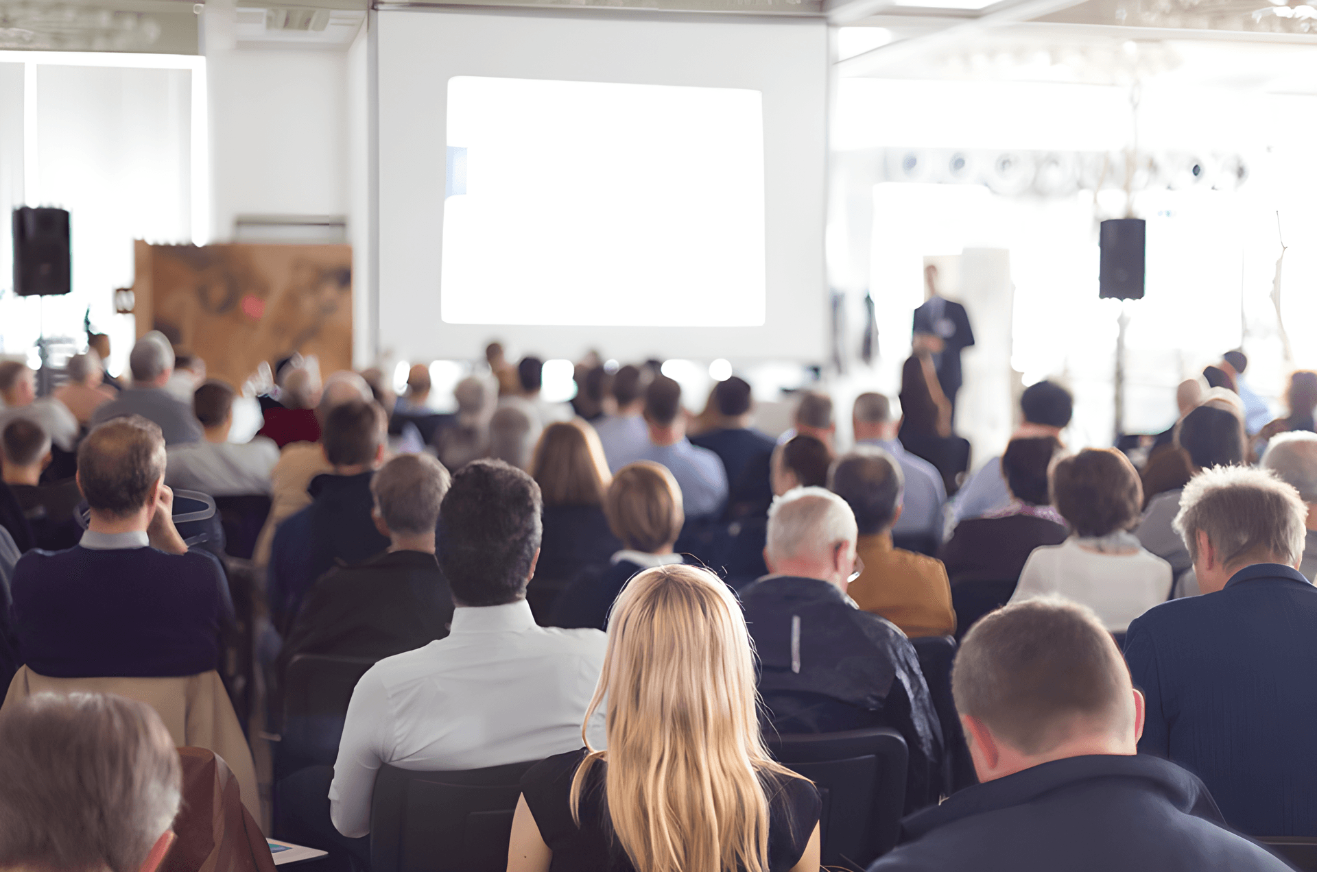 Conference audience facing a presentation screen with PA speakers on stands — seminar sound system rental